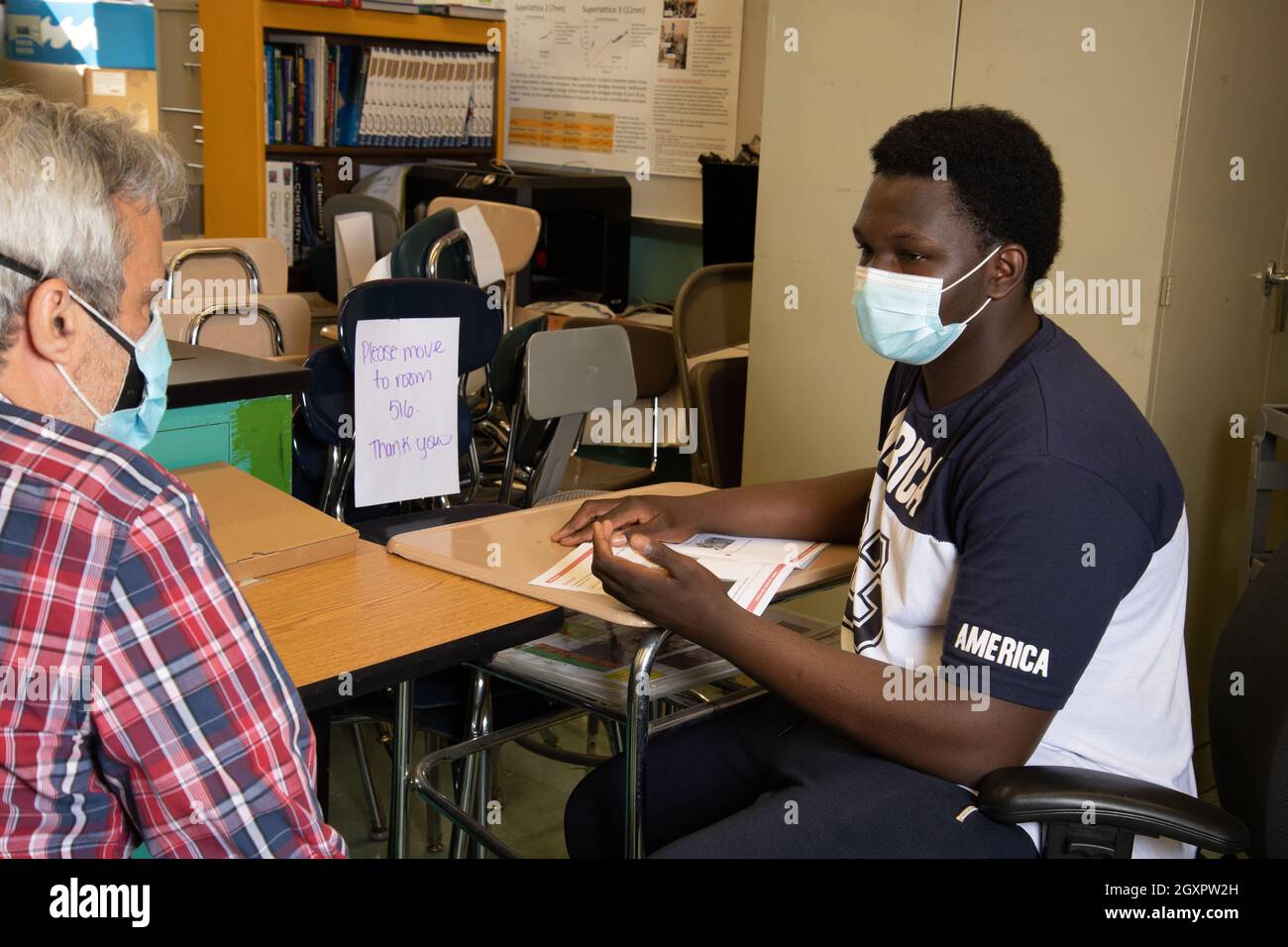 Education High School classroom scene male teacher talking with male student, both wearing face masks to protect against Covid-19 infection Stock Photo
