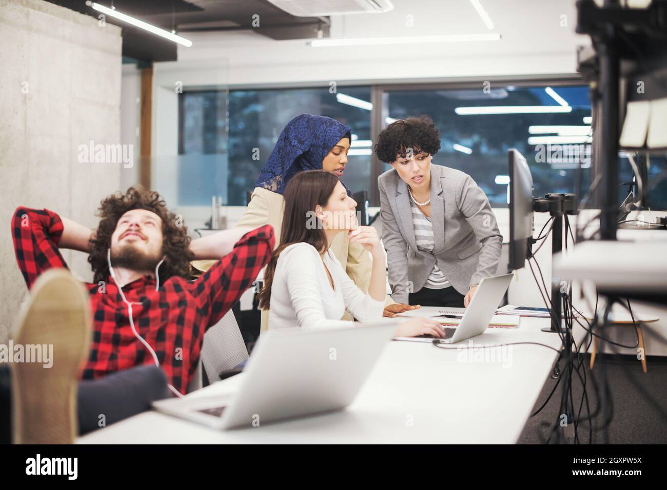young software developer resting with legs on desk while his multiethnics business team writing programming code in the background at startup office Stock Photo