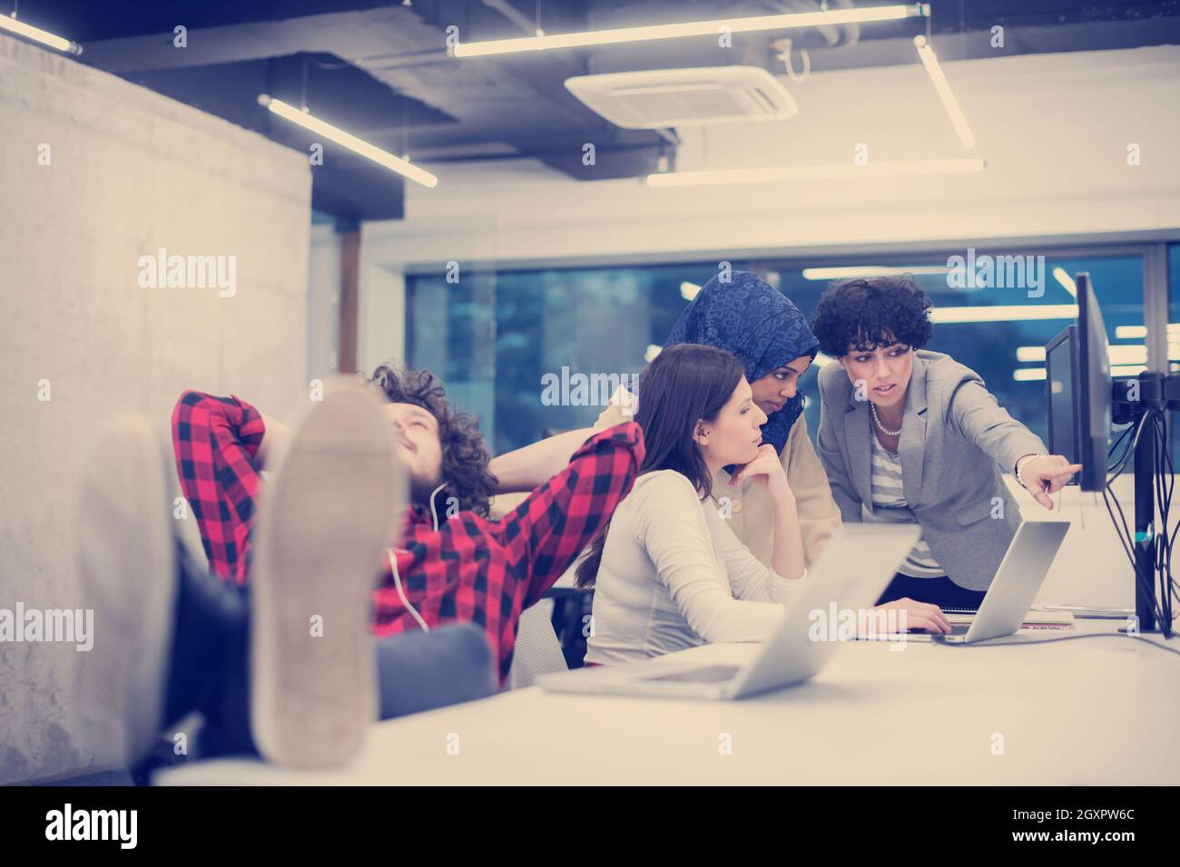 young software developer resting with legs on desk while his multiethnics business team writing programming code in the background at startup office Stock Photo