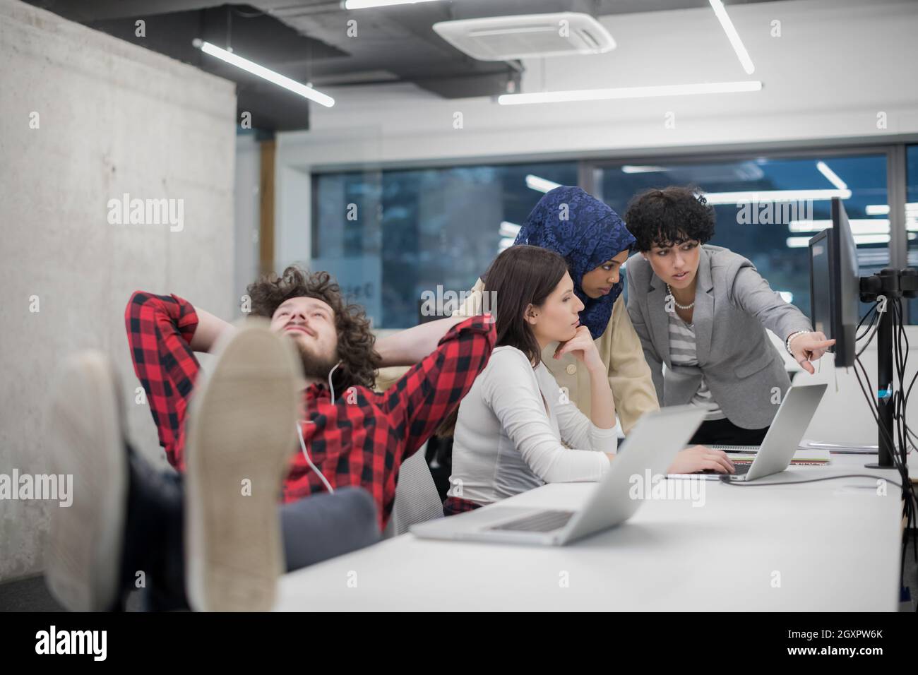 young software developer resting with legs on desk while his multiethnics business team writing programming code in the background at startup office Stock Photo