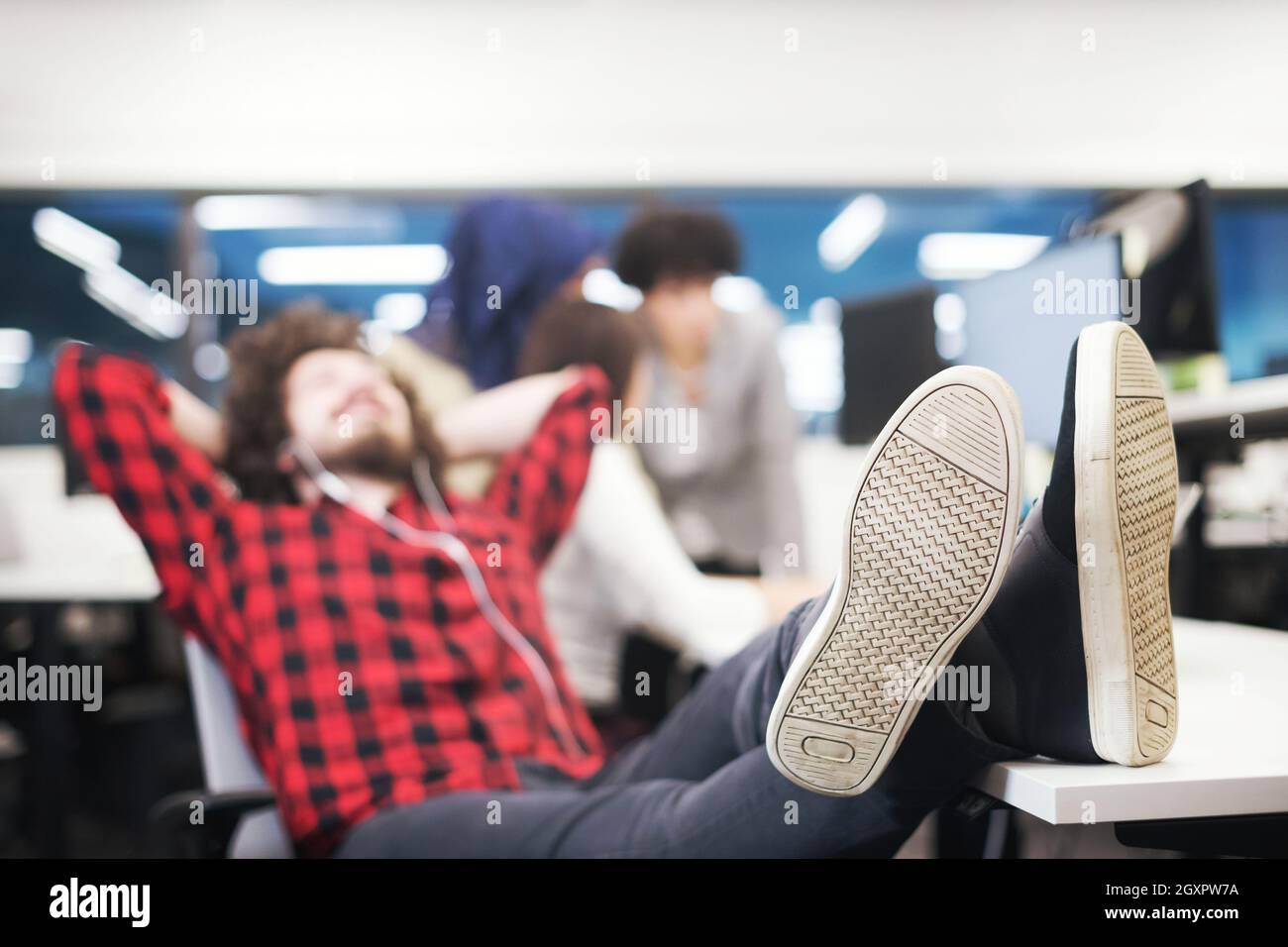 young software developer resting with legs on desk while his multiethnics business team writing programming code in the background at startup office Stock Photo