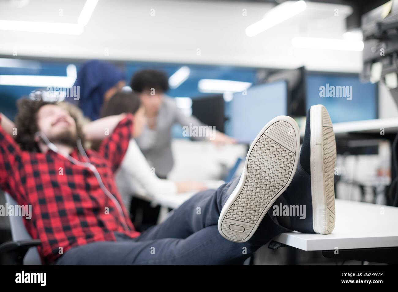 young software developer resting with legs on desk while his multiethnics business team writing programming code in the background at startup office Stock Photo