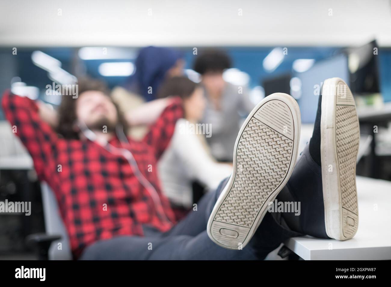 young software developer resting with legs on desk while his multiethnics business team writing programming code in the background at startup office Stock Photo