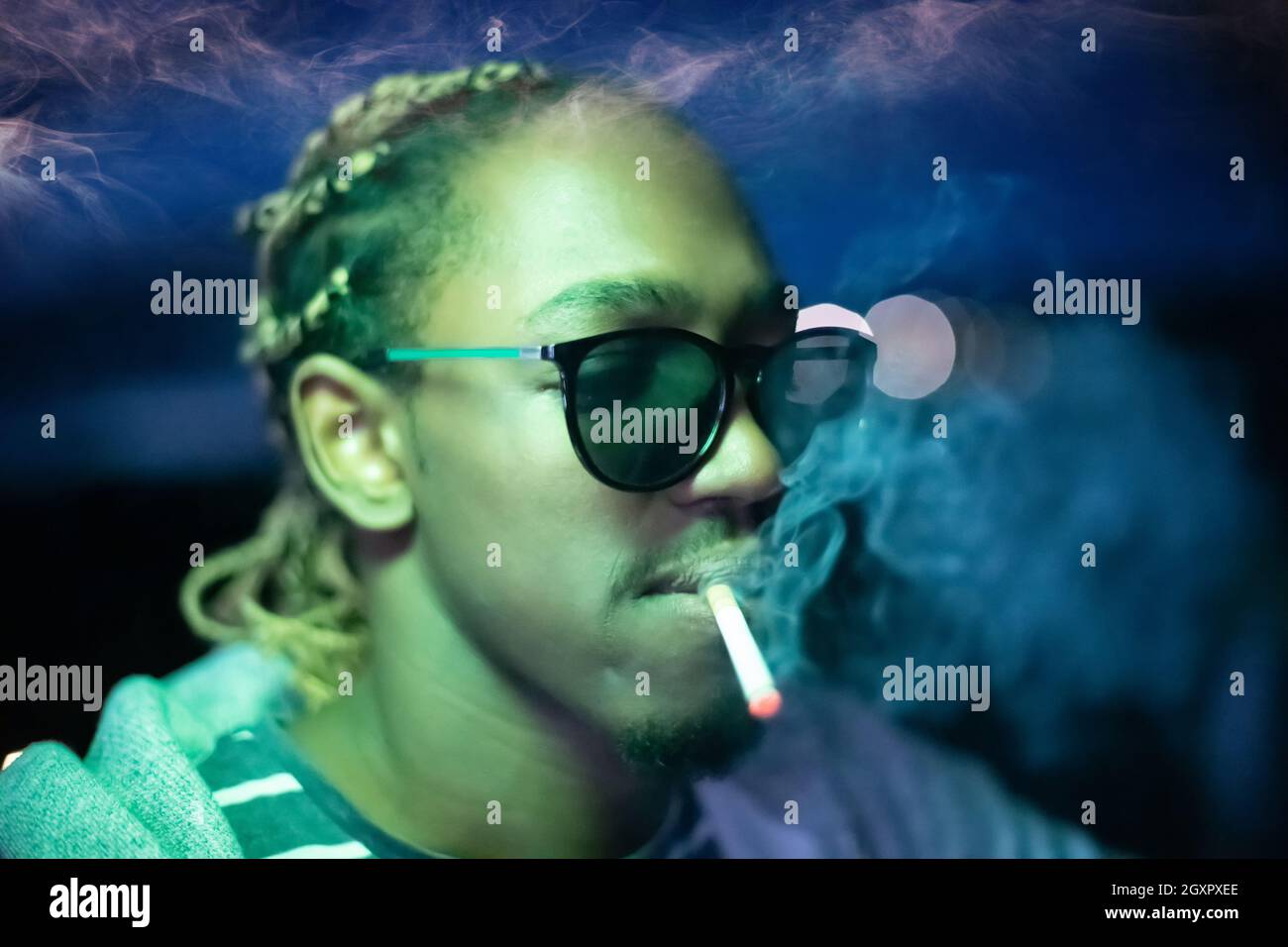 disco cigarette Young African American man smoking cigarette with neon lights and disco  party at night Stock Photo