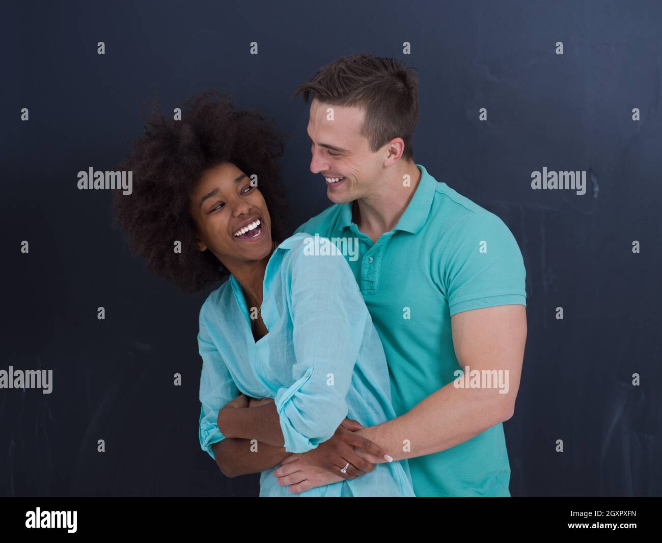 Young happy multiethnic couple laughing and hugging in front of gray ...