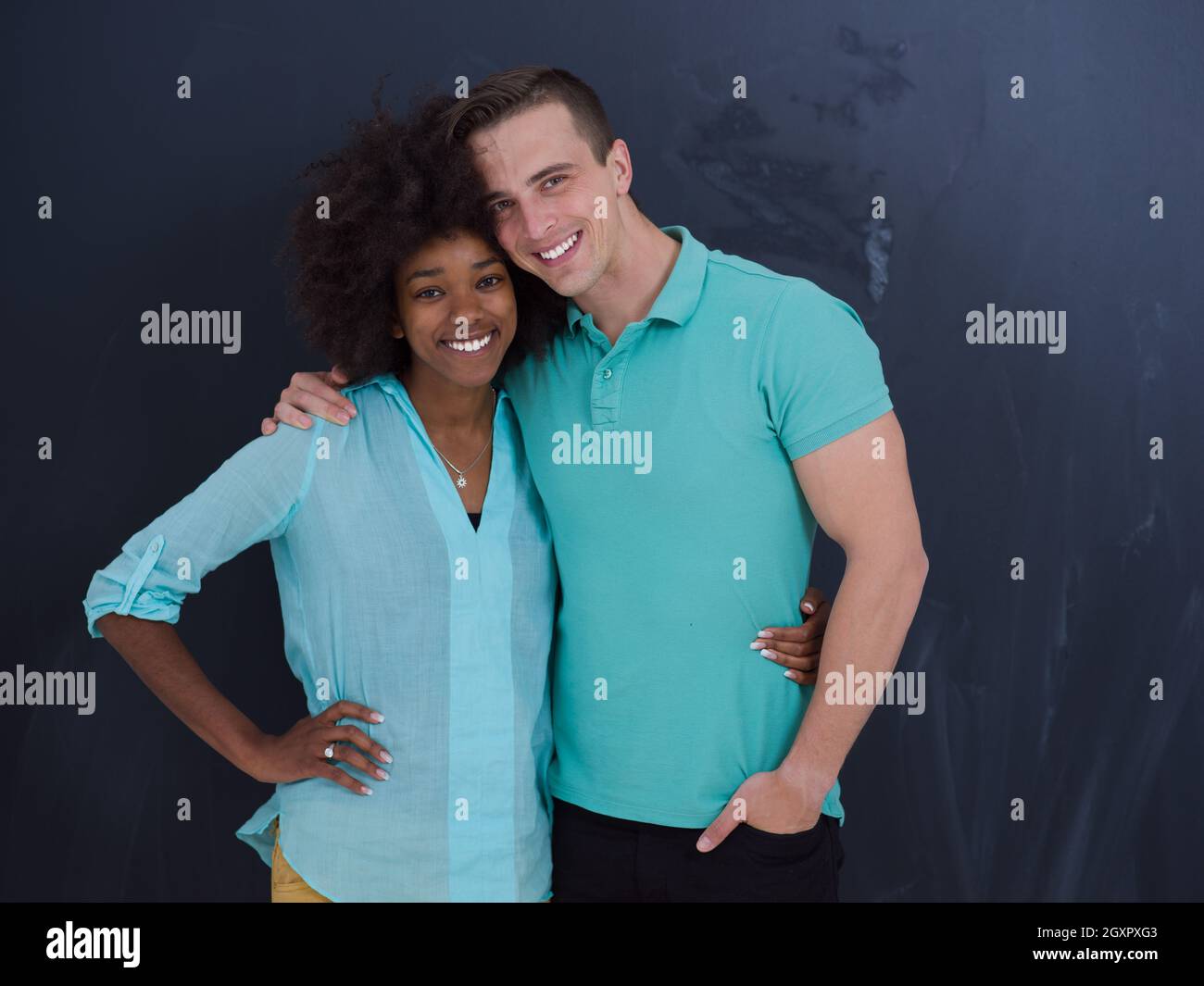 Young happy multiethnic couple laughing and hugging in front of gray ...