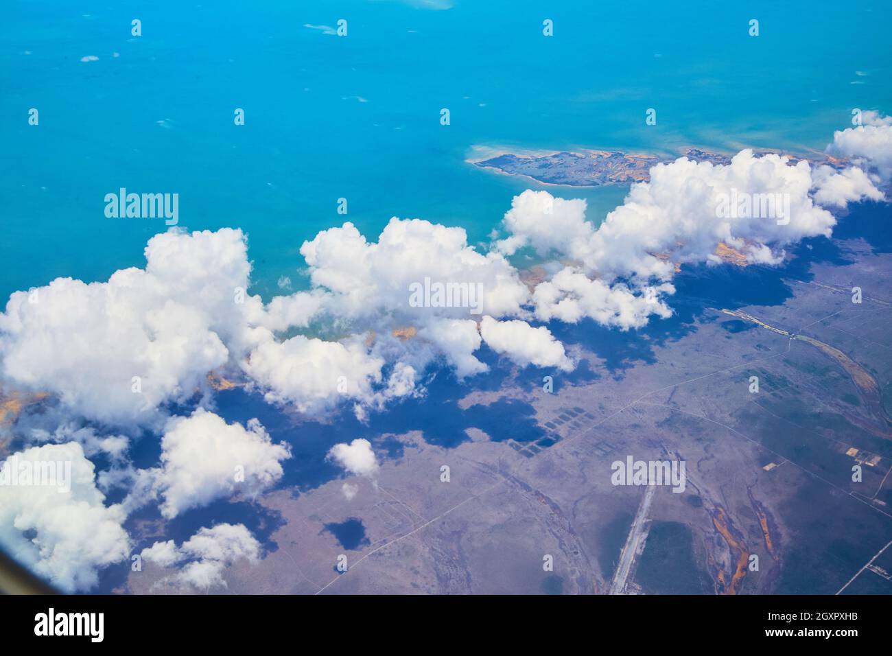 Large white clouds from airplane over land with colorful ocean view Stock Photo