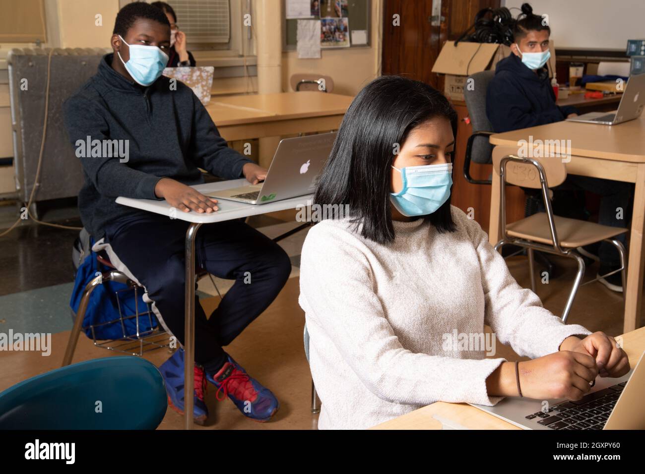 Education High School classroom scene, female & male students sit in classroom with laptop computers, listening, wearing masks to protect vs Covid-19 Stock Photo