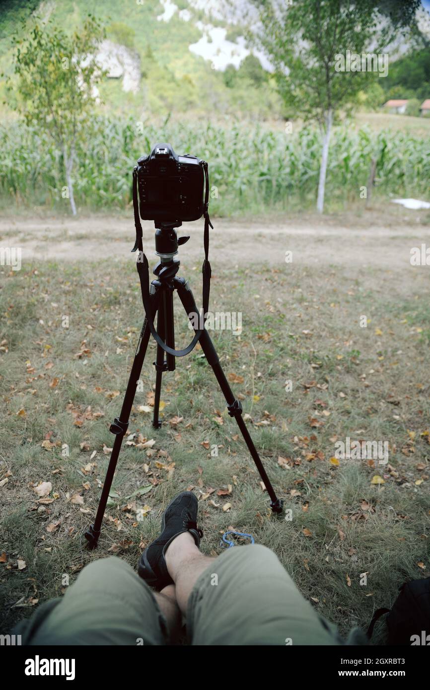 pov photographer in nature taking timelapse photo on pro dslr camera with tripod while sitting in chair and relaxing Stock Photo