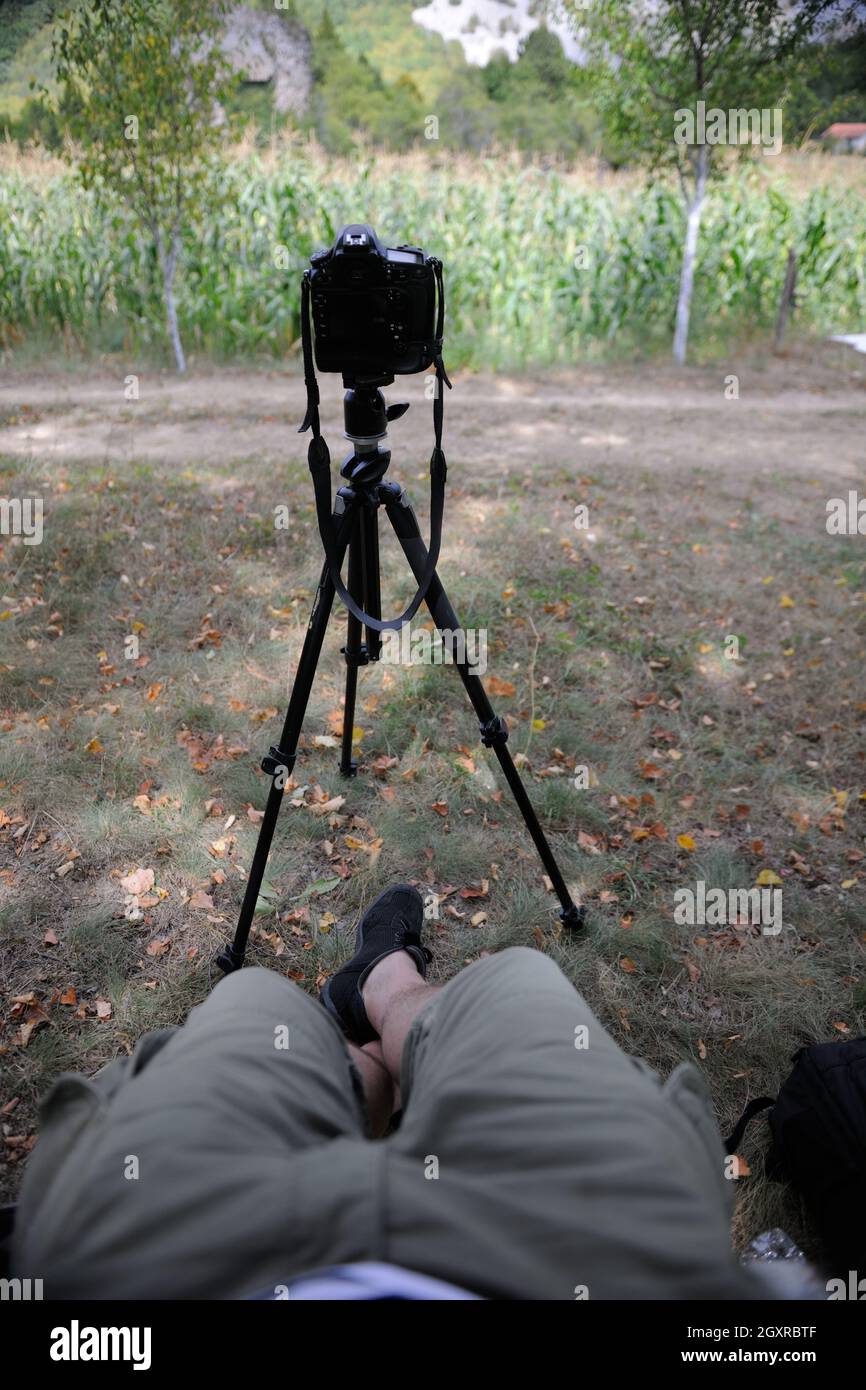 pov photographer in nature taking timelapse photo on pro dslr camera with tripod while sitting in chair and relaxing Stock Photo