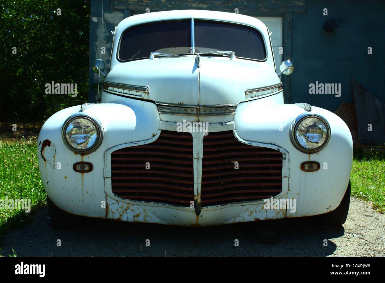 Head-on shot of a clean white vintage car flanked by grass on either side Stock Photo