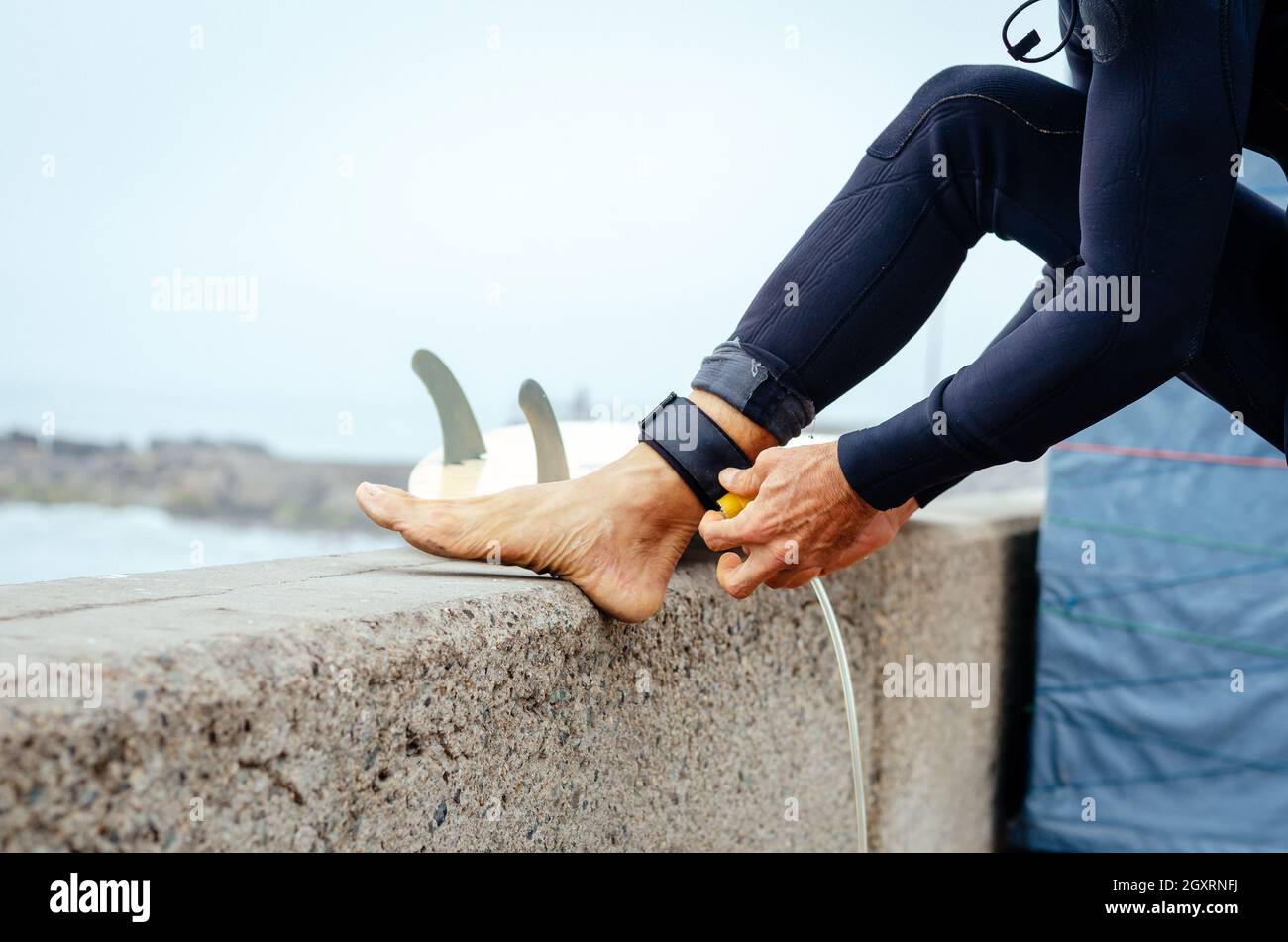 Closeup of young man putting on surfboard leash on beach. Guy wearing