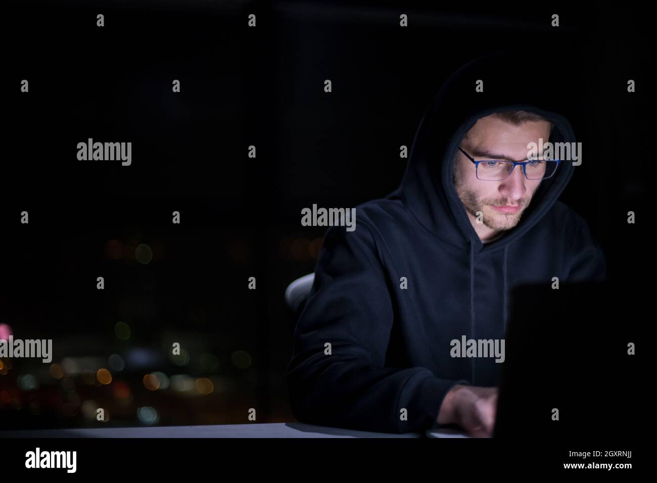 Young talented hacker using laptop computer while working in dark ...