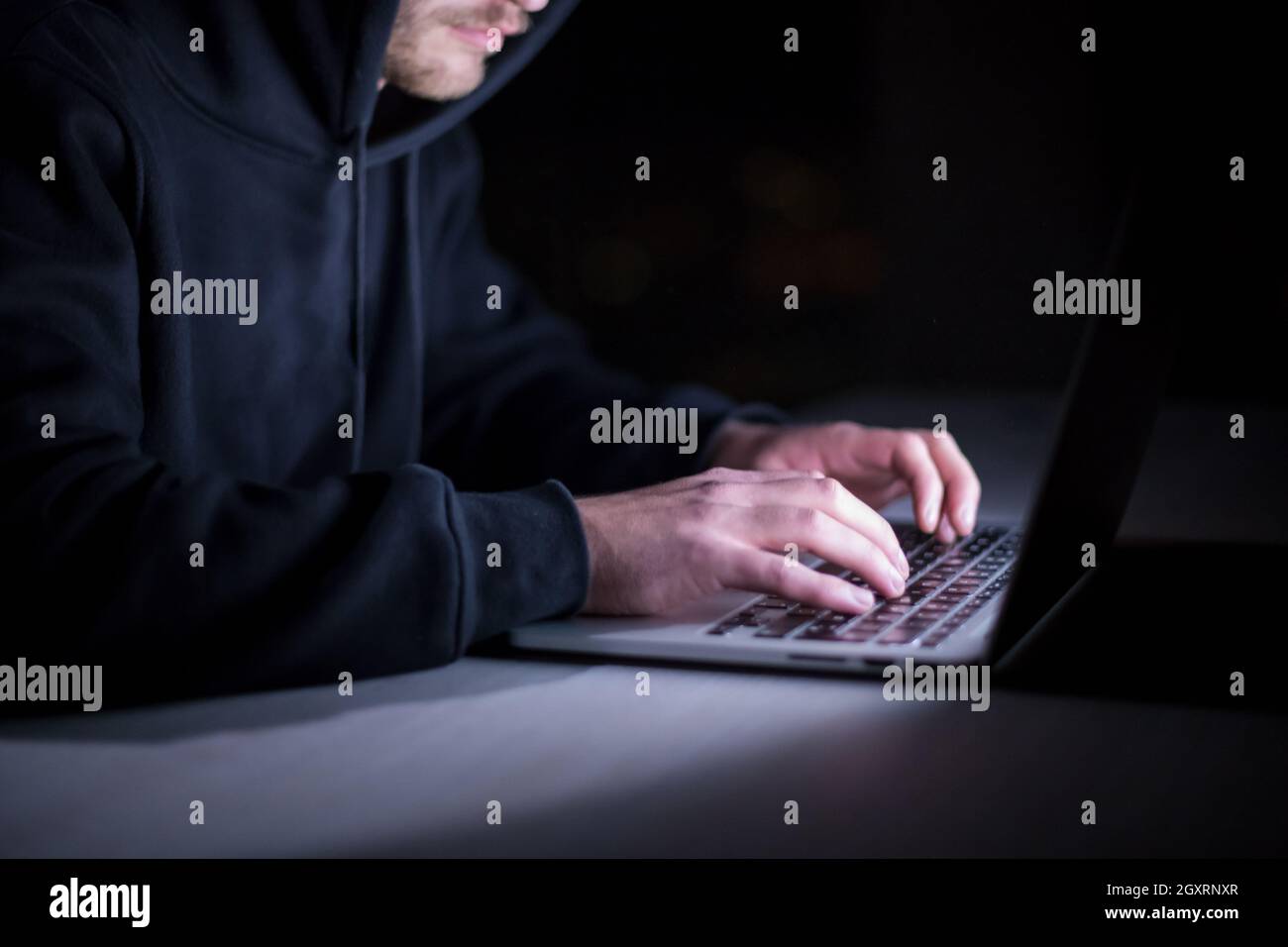 Young talented hacker using laptop computer while working in dark ...