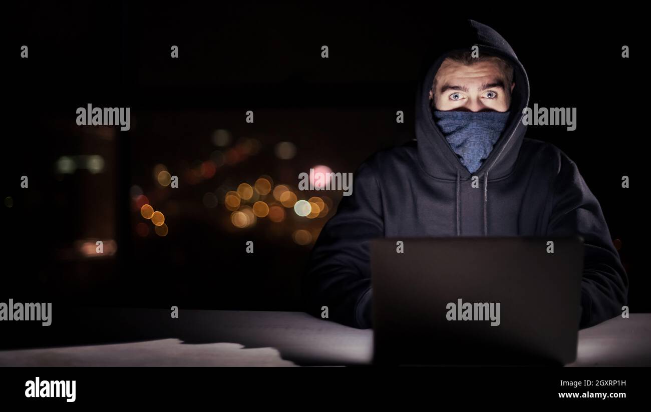 Young talented hacker using laptop computer while working in dark ...