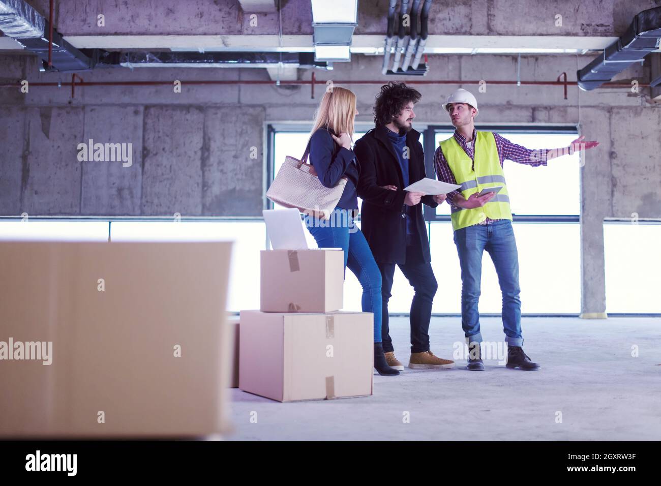architect using tablet computer while showing house design plans to a young couple at construction site Stock Photo