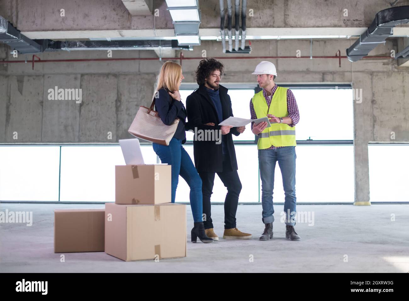 architect using tablet computer while showing house design plans to a young couple at construction site Stock Photo