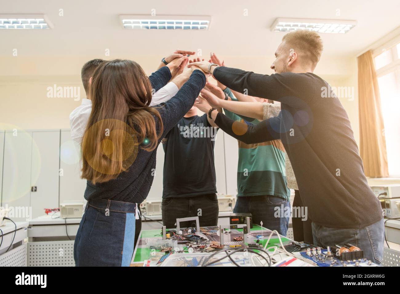 Group of young students in electronics classroom celebrating successfully finished project with