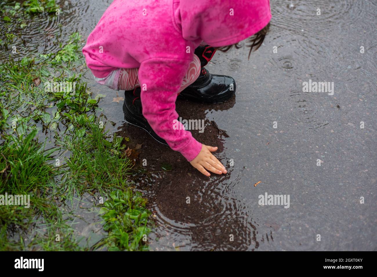 A young child plays on a sidewalk in the rain while wearing pink. Stock Photo