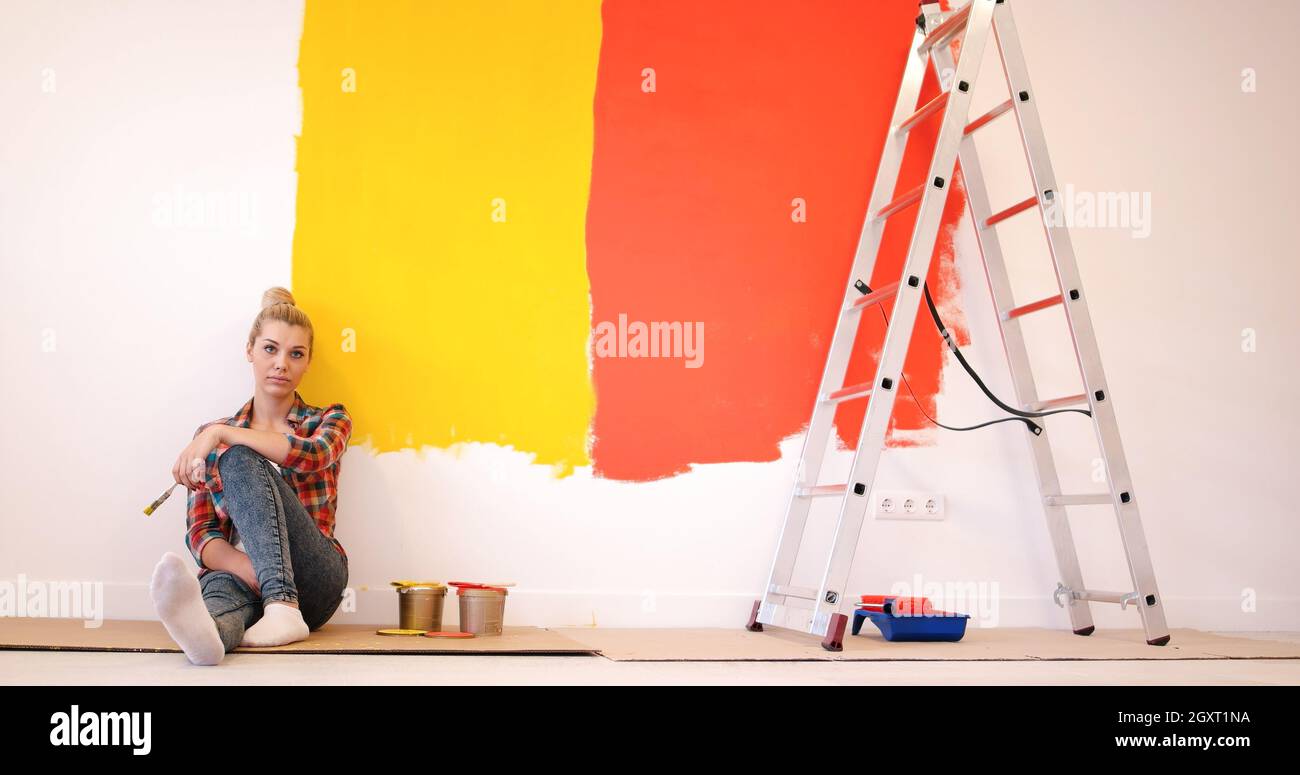 Portrait of a beautiful young female painter sitting on floor near wall ...