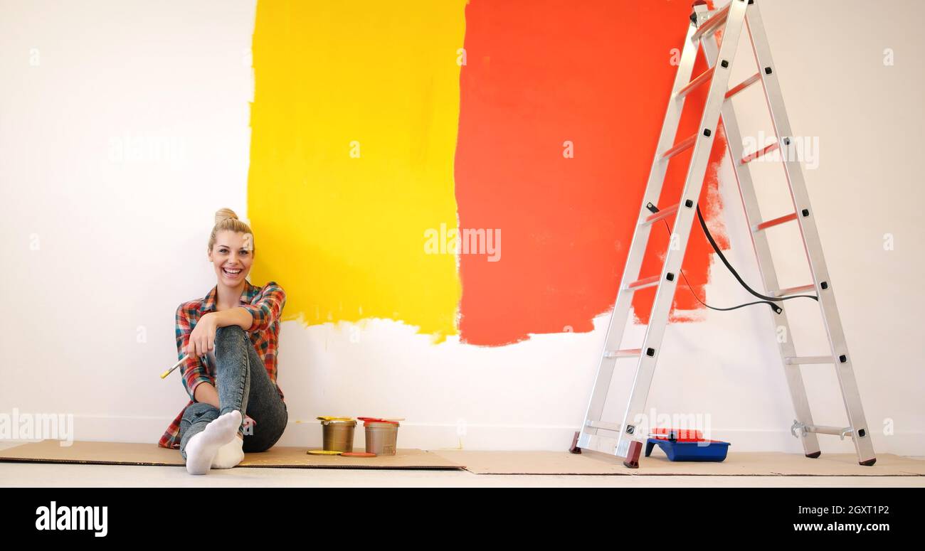 Portrait of a beautiful young female painter sitting on floor near wall ...