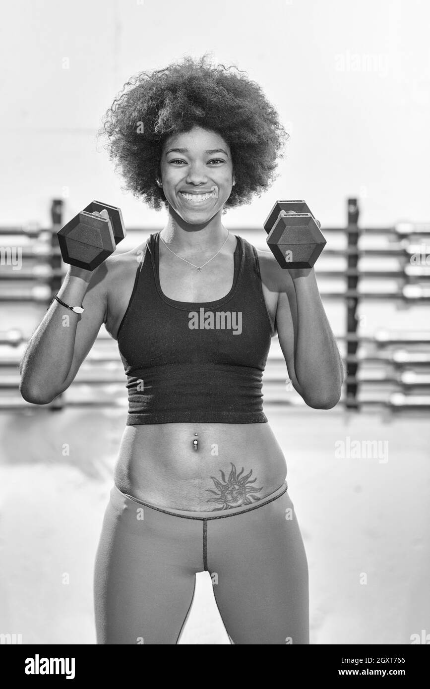 young beautiful African American woman doing bicep curls in a gym Stock Photo