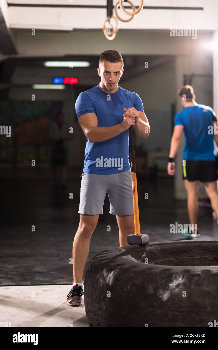Sledgehammer Tire Hits young muscular man workout at gym with hammer and tractor tire Stock