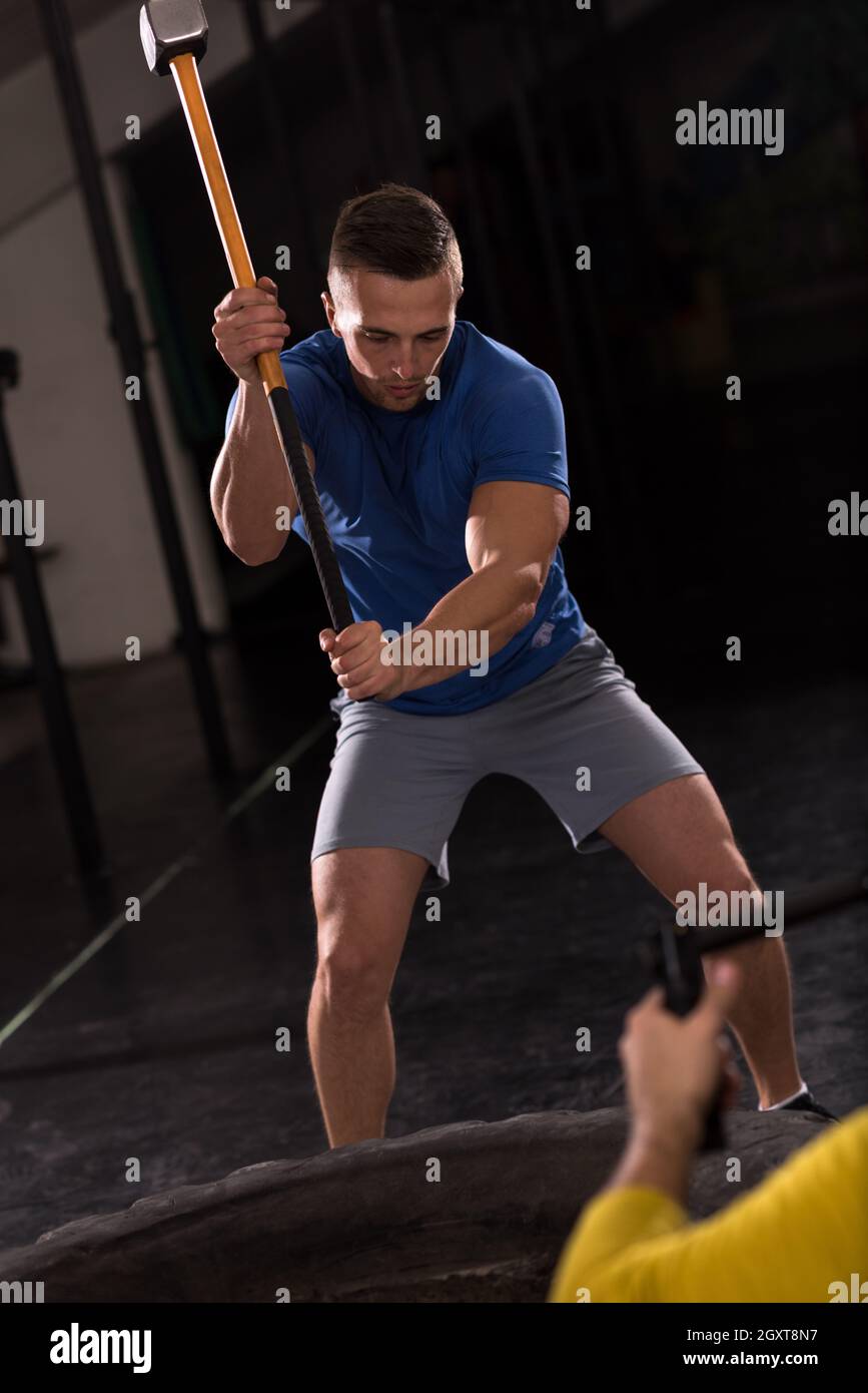 Sledgehammer Tire Hits young muscular man workout at gym with hammer and tractor tire Stock