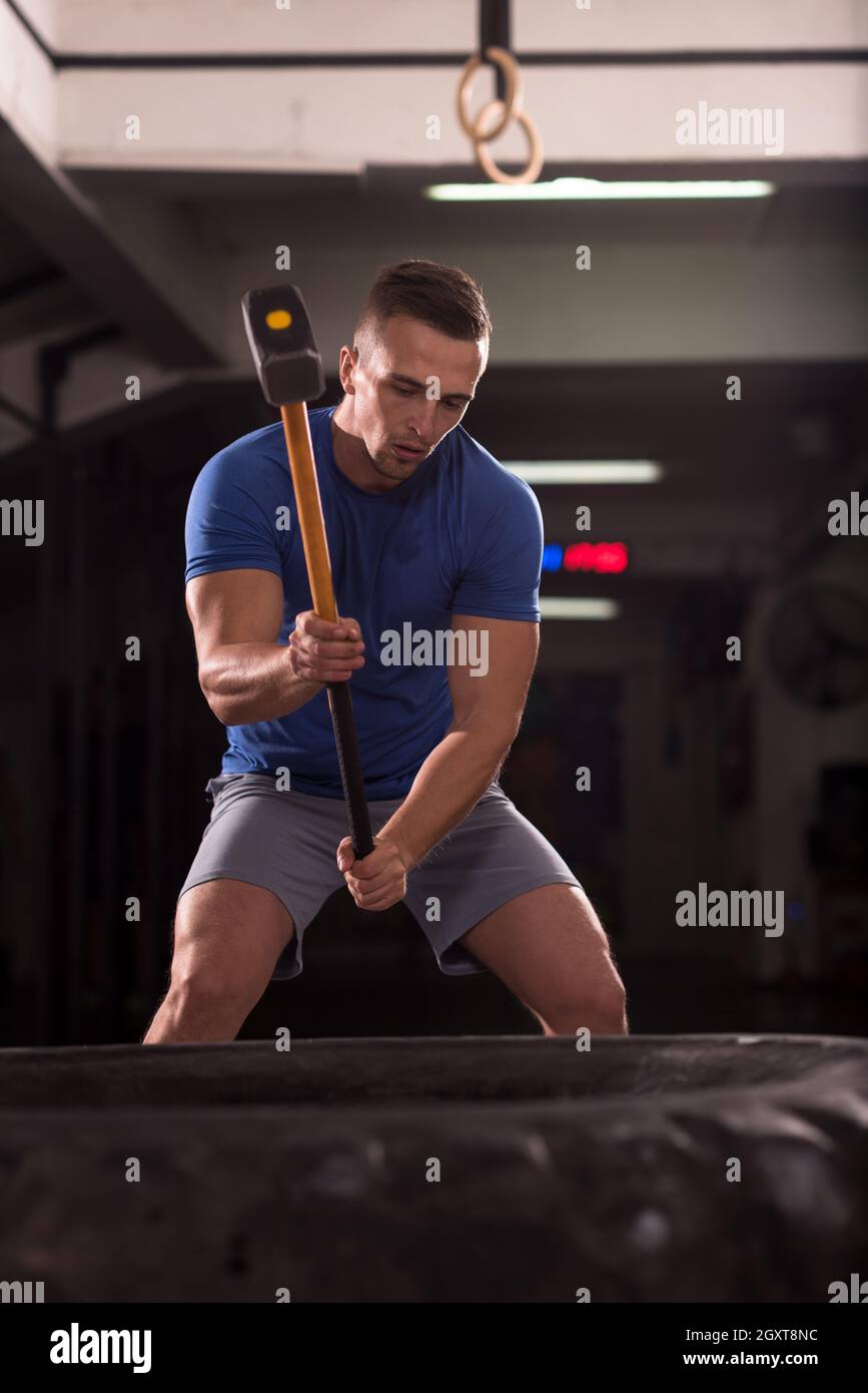 Sledgehammer Tire Hits young muscular man workout at gym with hammer and tractor tire Stock
