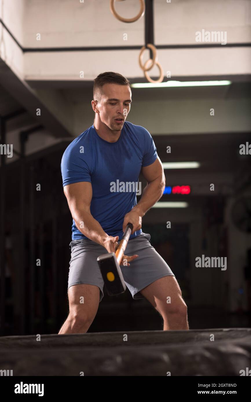 Sledgehammer Tire Hits young muscular man workout at gym with hammer and tractor tire Stock