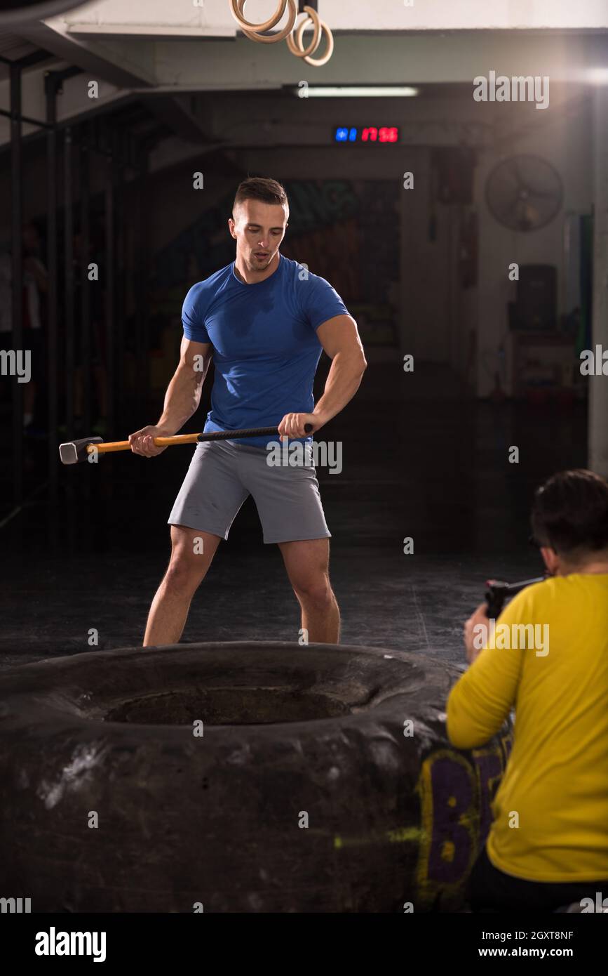 Sledgehammer Tire Hits young muscular man workout at gym with hammer