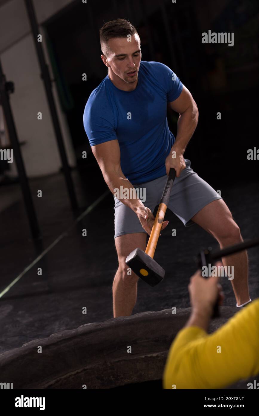 Sledgehammer Tire Hits young muscular man workout at gym with hammer and tractor tire Stock