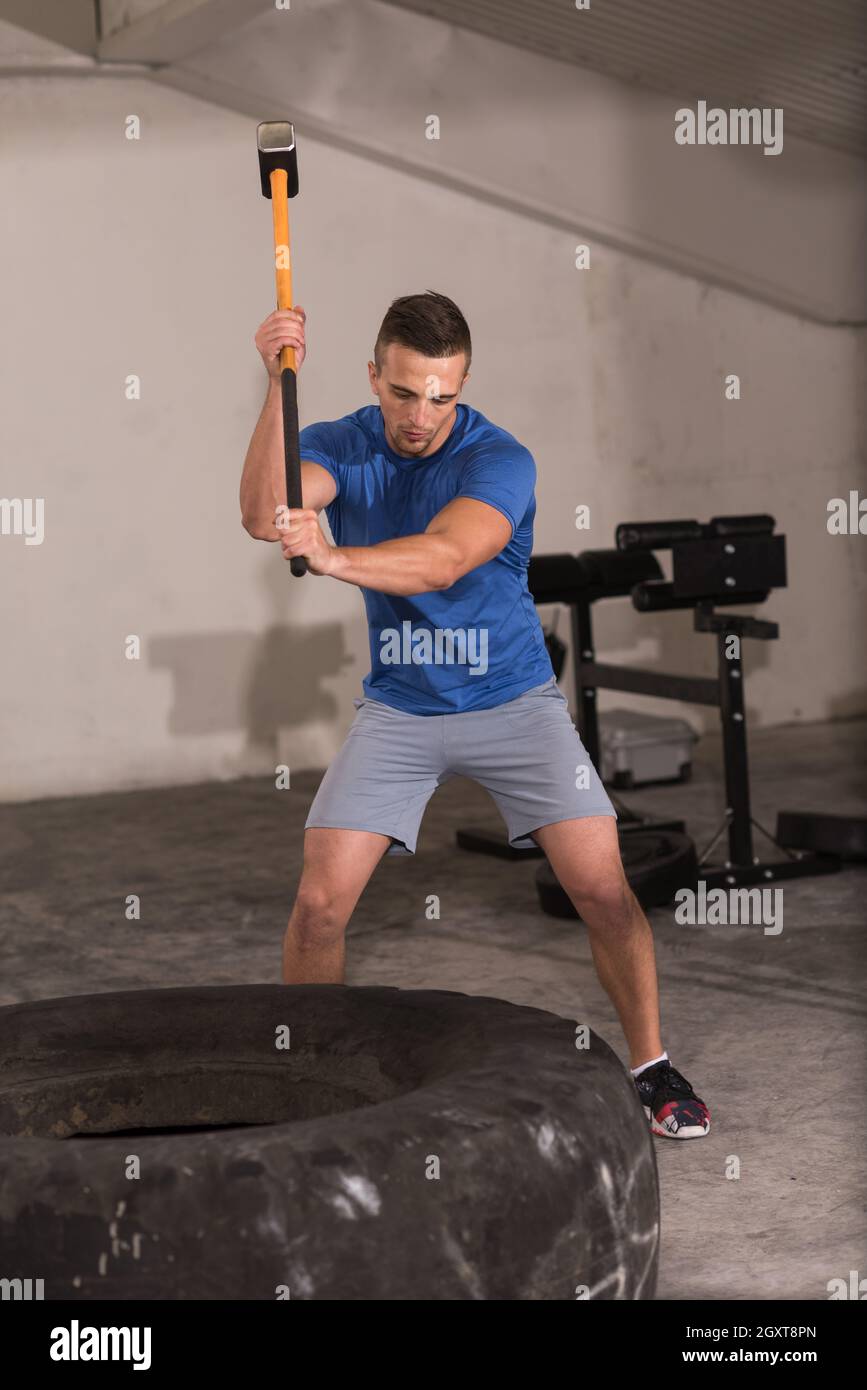 Sledgehammer Tire Hits young muscular man workout at gym with hammer