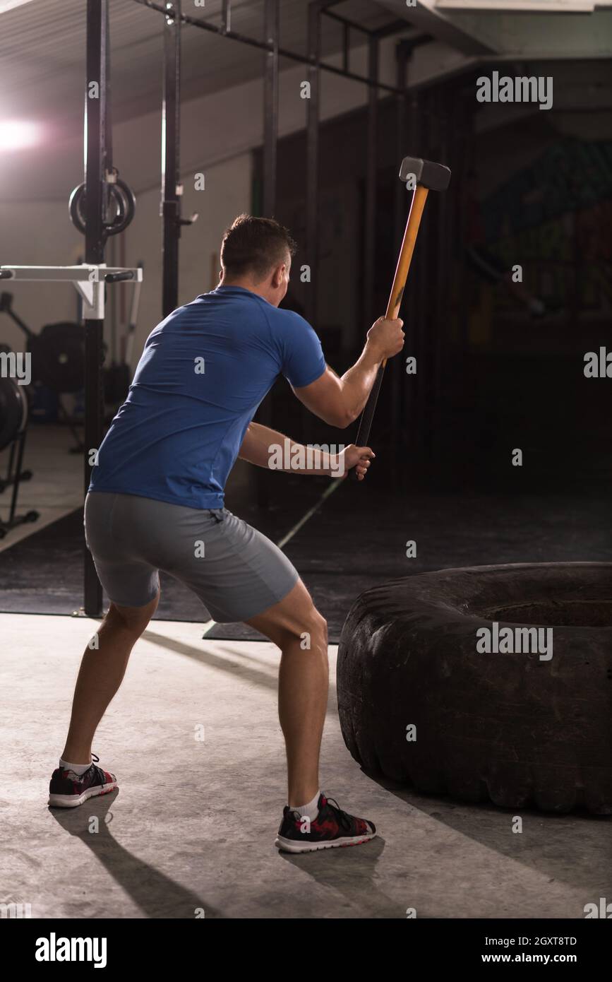 Sledgehammer Tire Hits young muscular man workout at gym with
