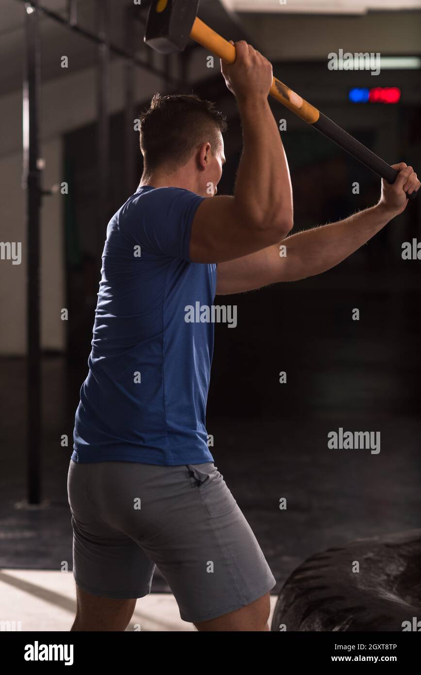 Sledgehammer Tire Hits young muscular man workout at gym with hammer and tractor tire Stock