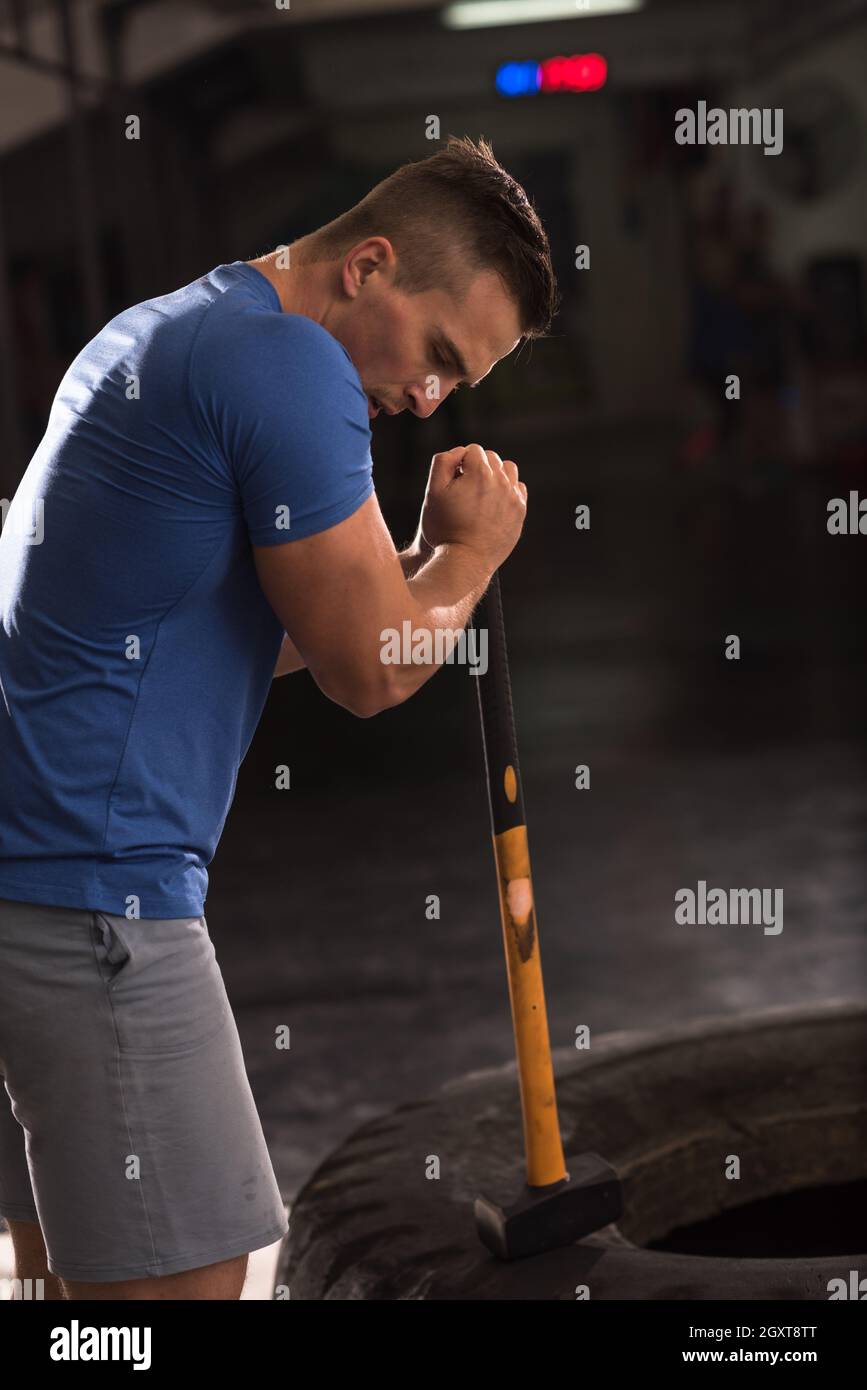 Sledgehammer Tire Hits young muscular man workout at gym with hammer