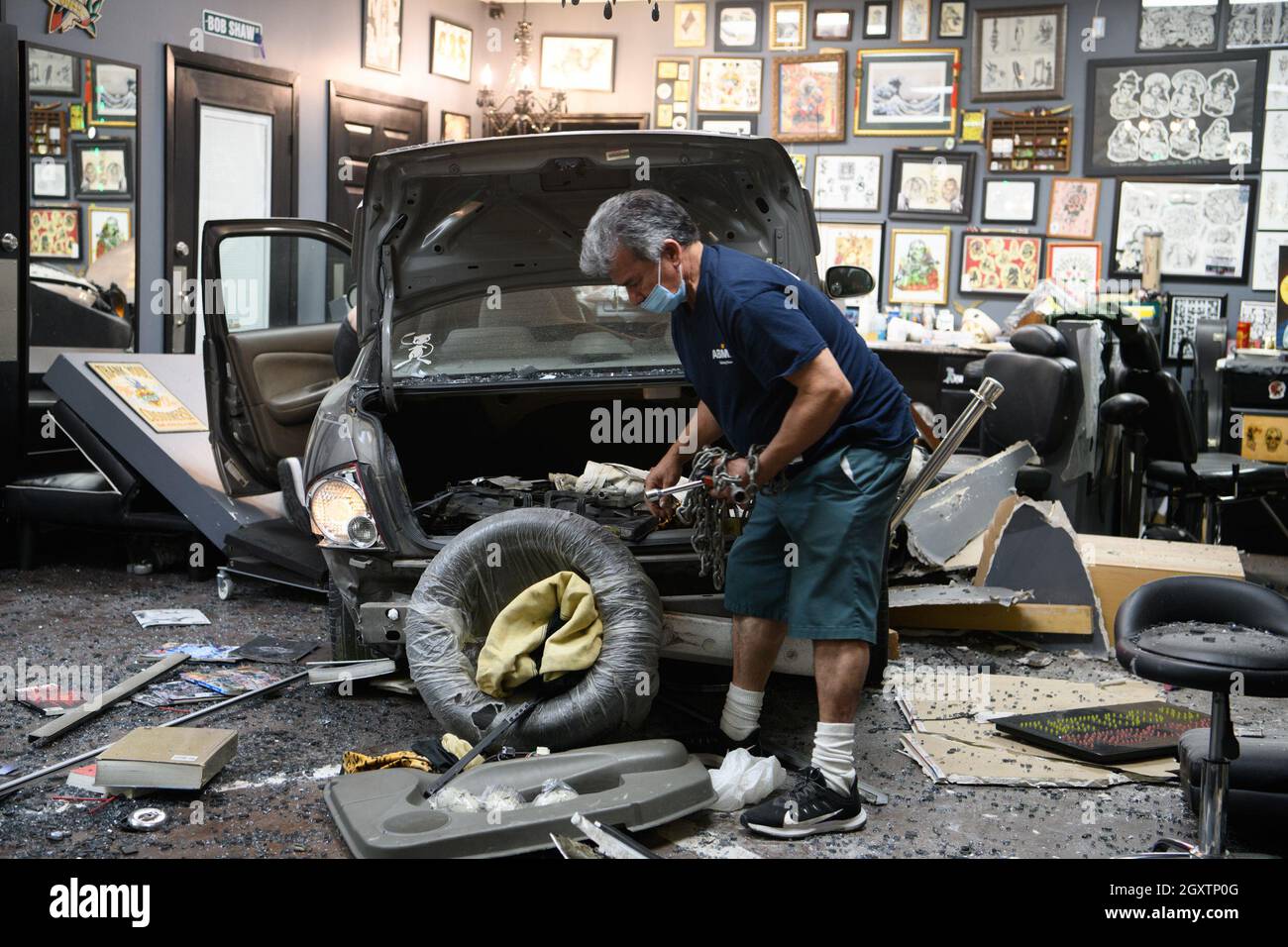 October 5, 2021: A car slammed into the Stainless Studios - Custom Tattoo Parlor in Dallas TX after being struck by another car, destroying a customer sitting area and tattoo station.None of the shop's employees or the occupants of the car were injured. The shop manager said that if a customer had not cancelled her appointment for this evening, they would have been sitting in that station when the vehicle struck.The other car fled the scene, minus a bumper, and is being sought by the Dallas Police Department. The occupants of the errant vehicle take personal items out of the car befor Stock Photo