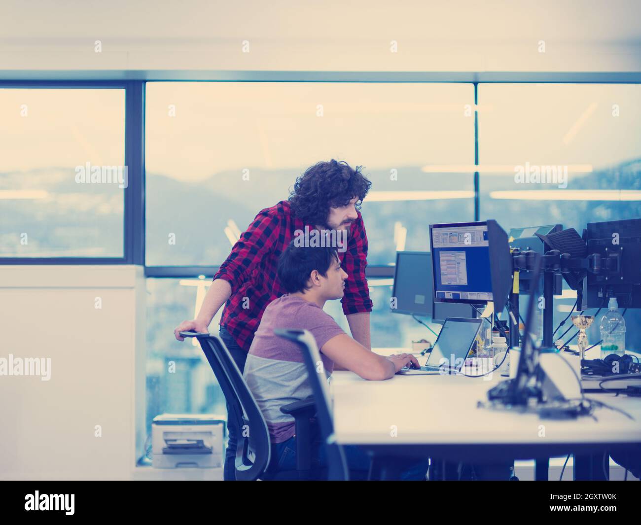 two young male software developers using laptop and desktop computer while writing programming code at modern creative startup office Stock Photo