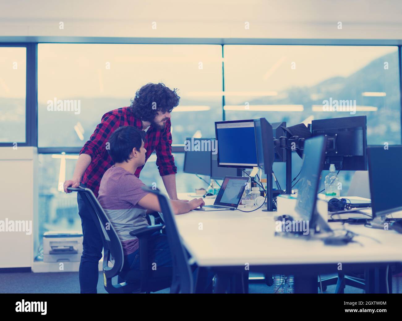 two young male software developers using laptop and desktop computer while writing programming code at modern creative startup office Stock Photo