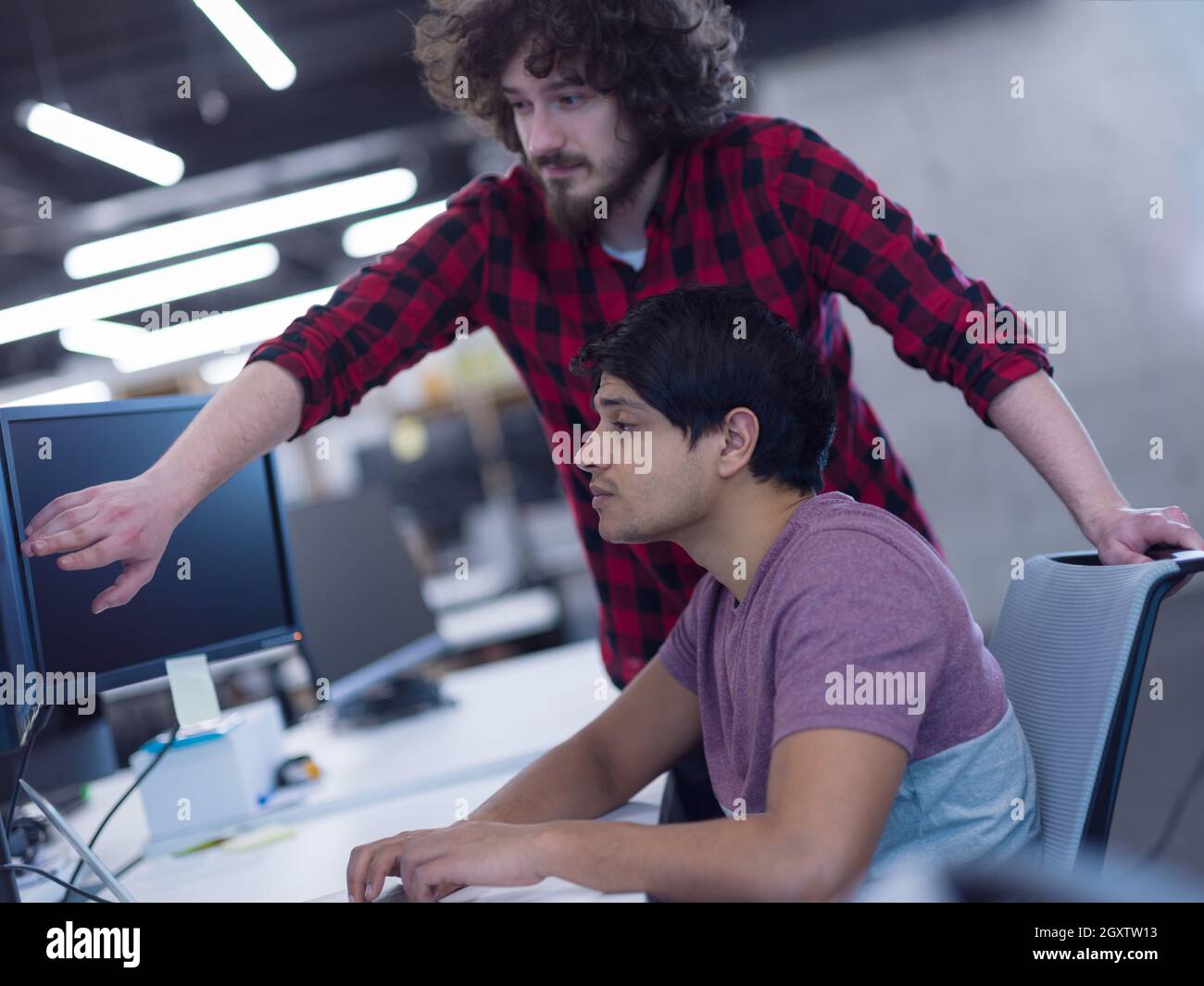 two young male software developers using laptop and desktop computer while writing programming code at modern creative startup office Stock Photo