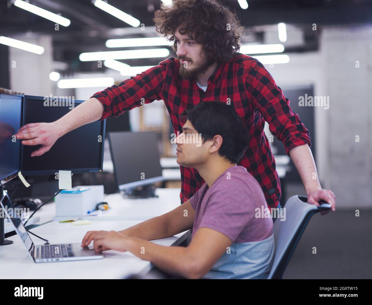 two young male software developers using laptop and desktop computer while writing programming code at modern creative startup office Stock Photo