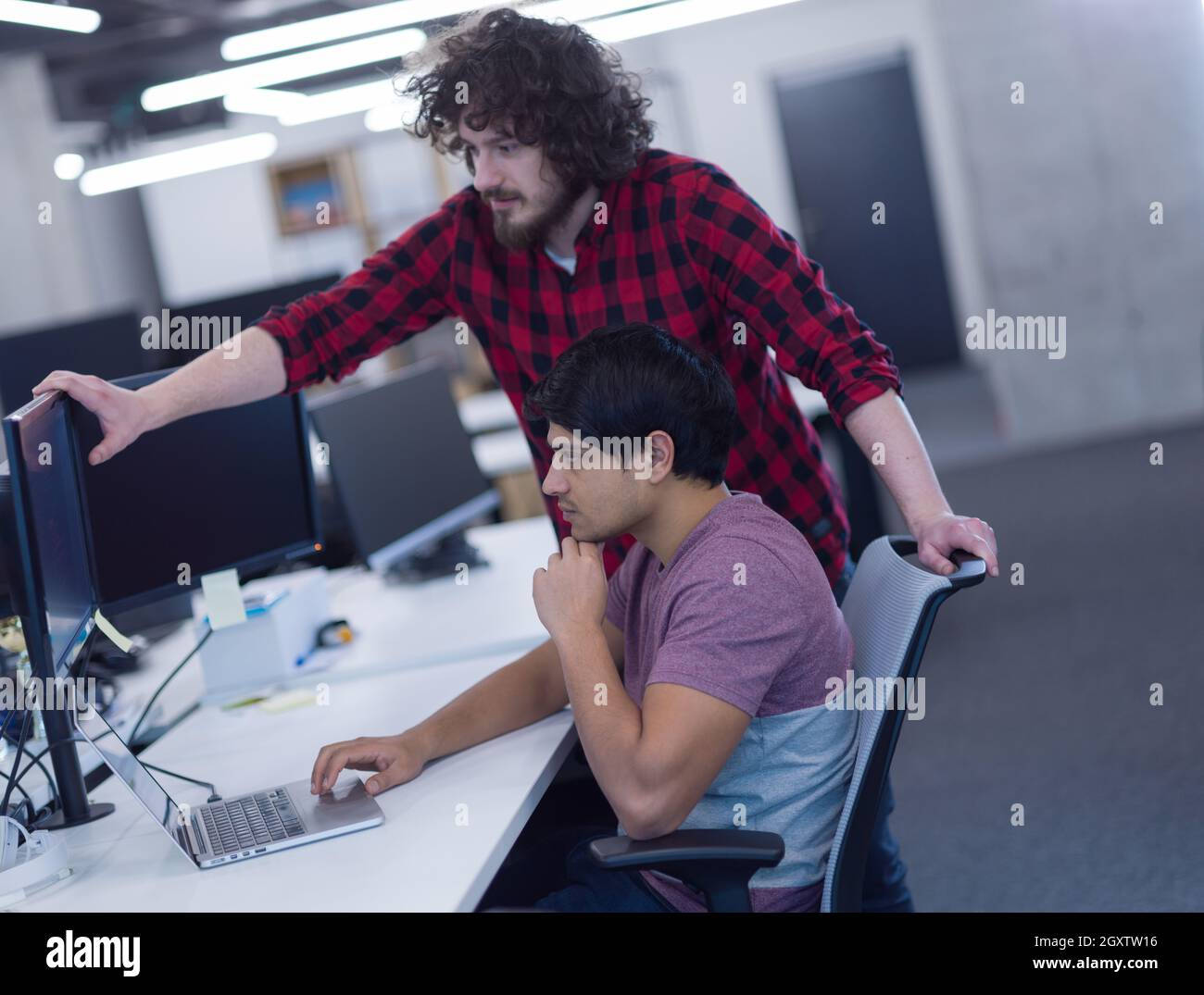 two young male software developers using laptop and desktop computer while writing programming code at modern creative startup office Stock Photo