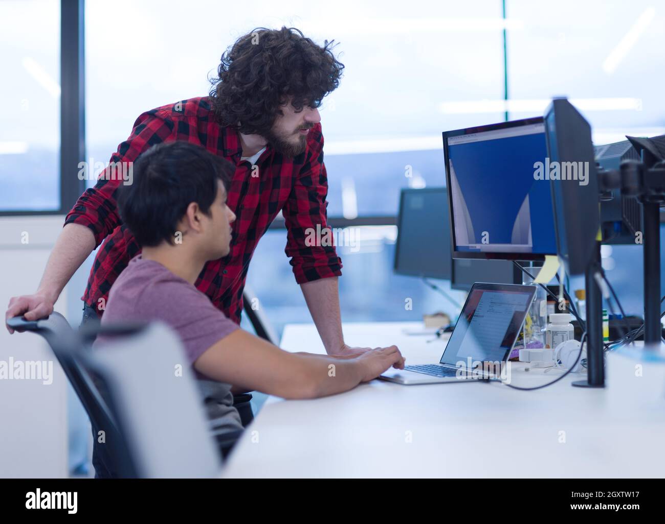 two young male software developers using laptop and desktop computer while writing programming code at modern creative startup office Stock Photo