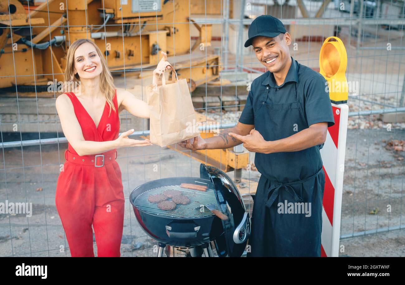 Cook handing woman customer a burger in bag for takeout in front of an unexplainable construction site Stock Photo