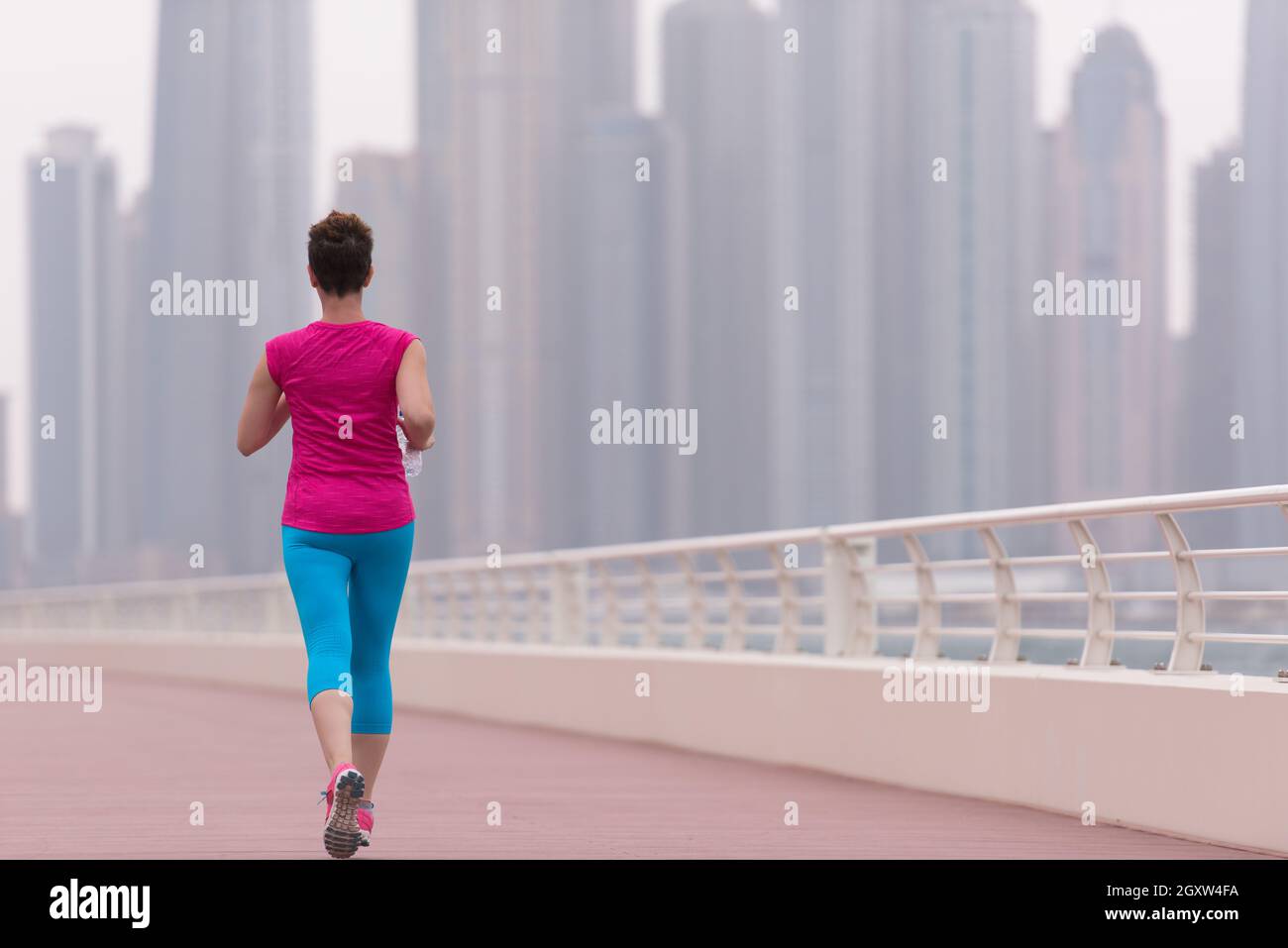 very active young beautiful woman busy running on the promenade along ...
