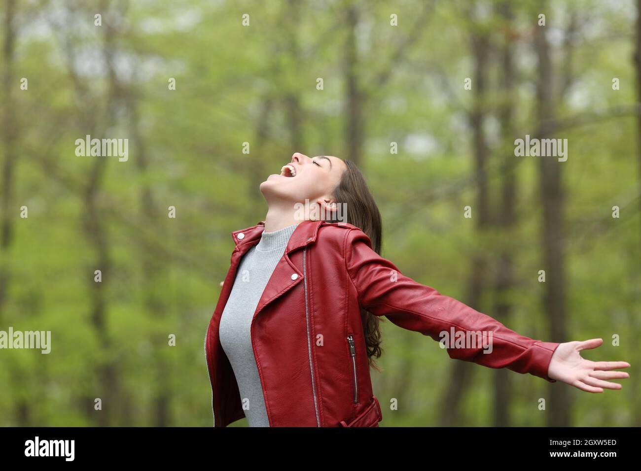 Excited woman in red spreding arms in a forest on vacation Stock Photo ...