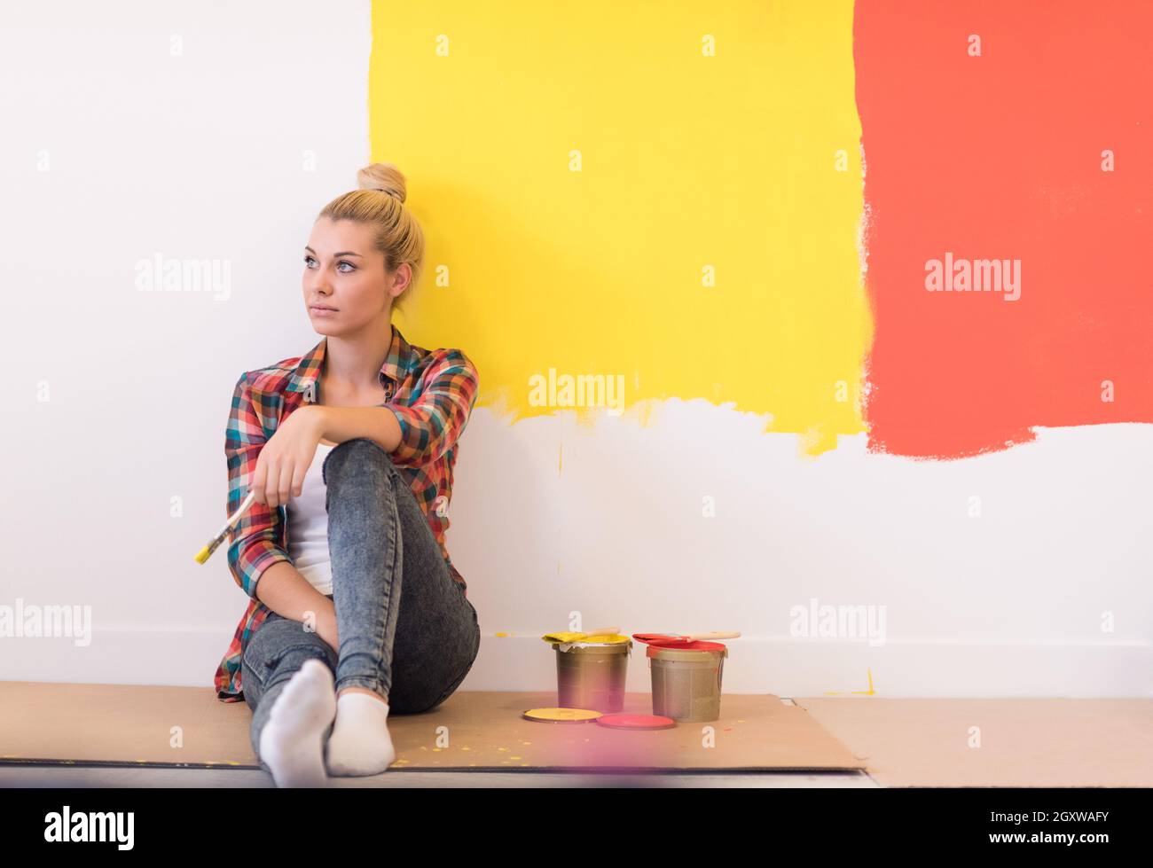 Portrait of a beautiful young female painter sitting on floor near wall ...