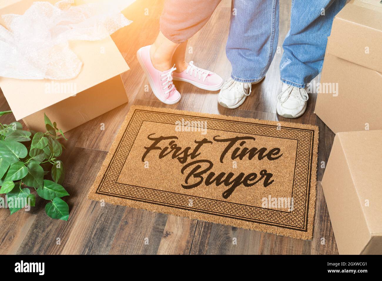 Man and Woman Unpacking Near Our First Time Buyer Welcome Mat, Moving Boxes and Plant. Stock Photo