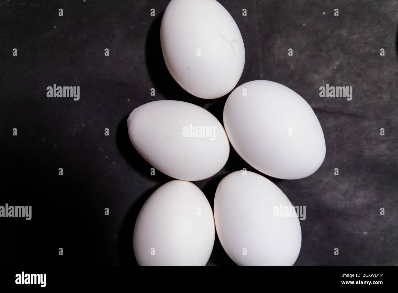 Five fresh white eggs lying down on black surface Stock Photo