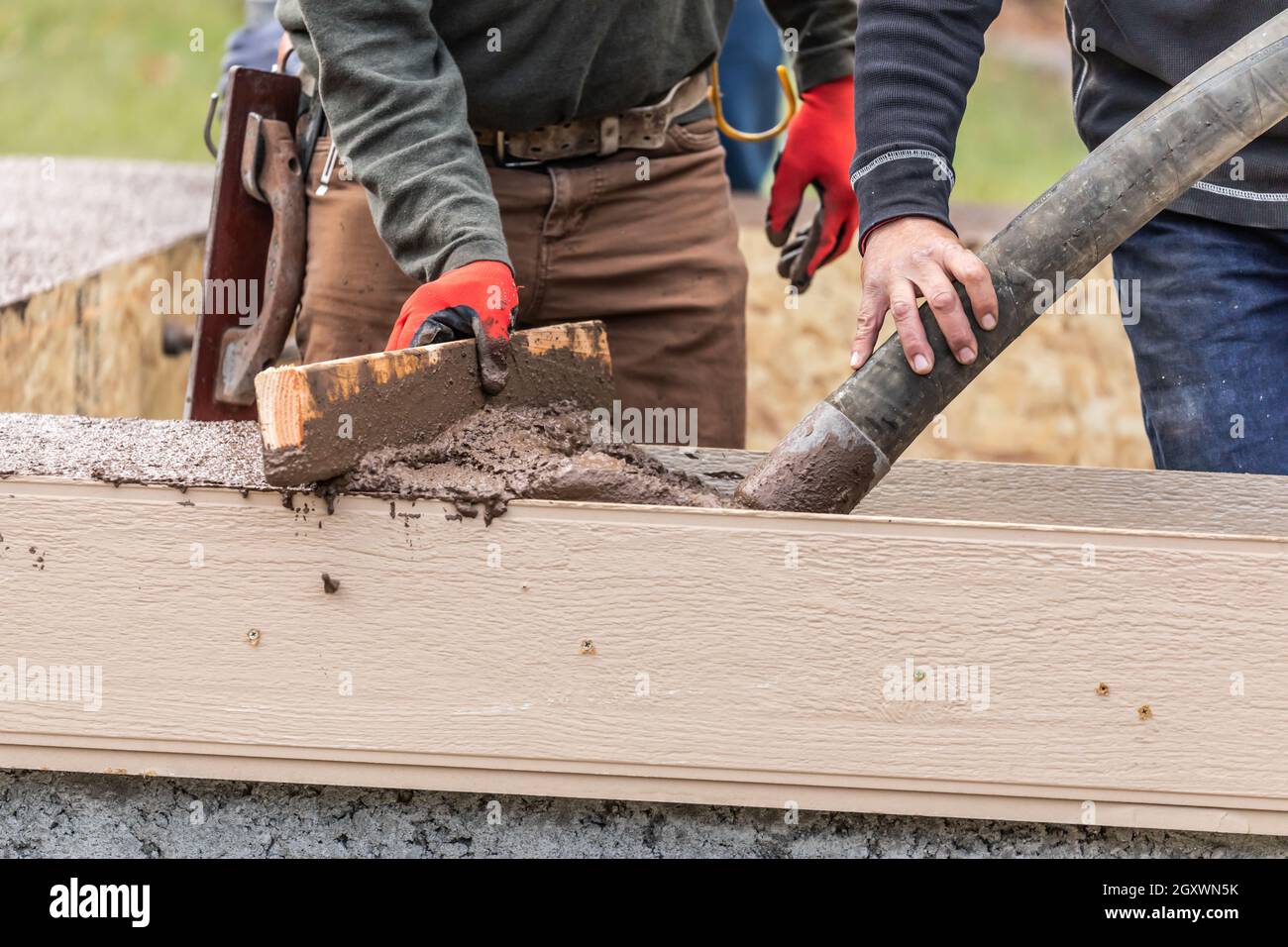 Construction Workers Pouring And Leveling Wet Cement Into Wood Framing